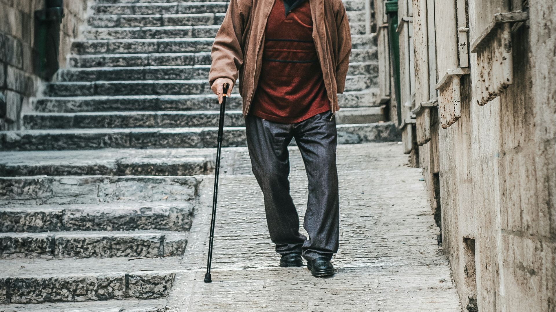Elderly man with cane walks down stone stairs.