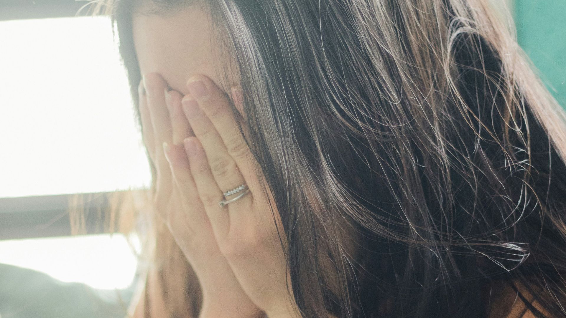 woman in brown shirt covering her face