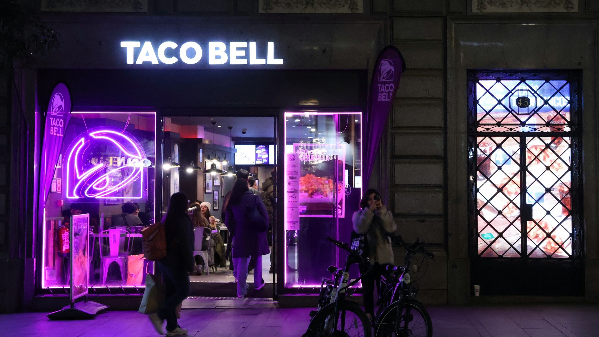 A purple lit store front with people walking by