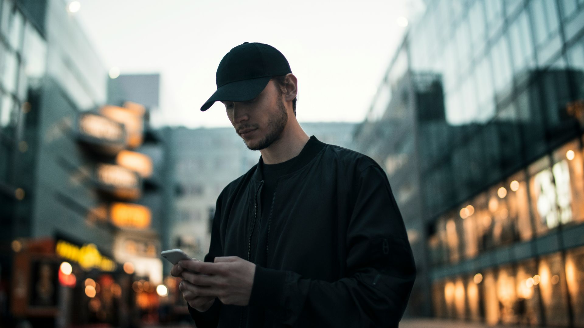 man in black jacket wearing black fitted cap while using phone