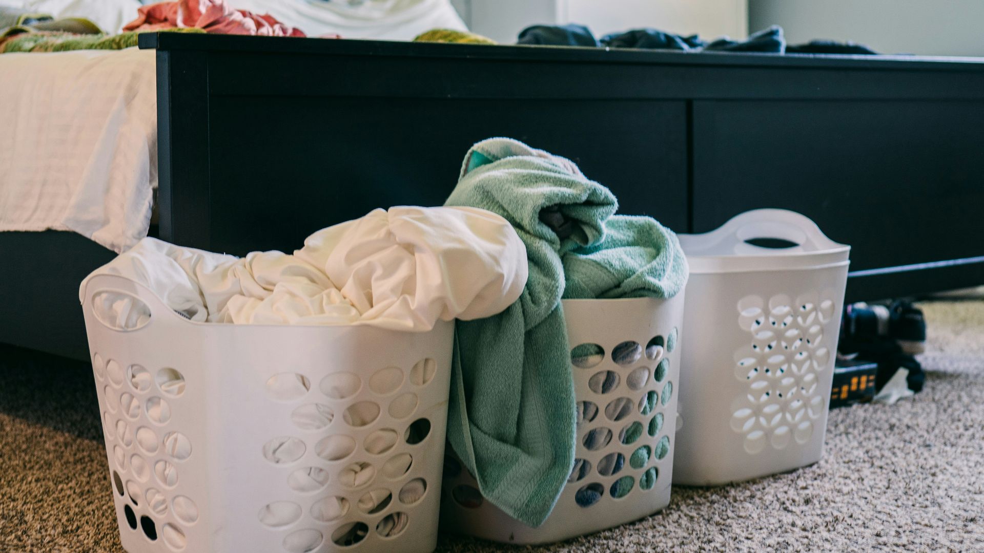 three laundry baskets sitting on the floor next to a bed