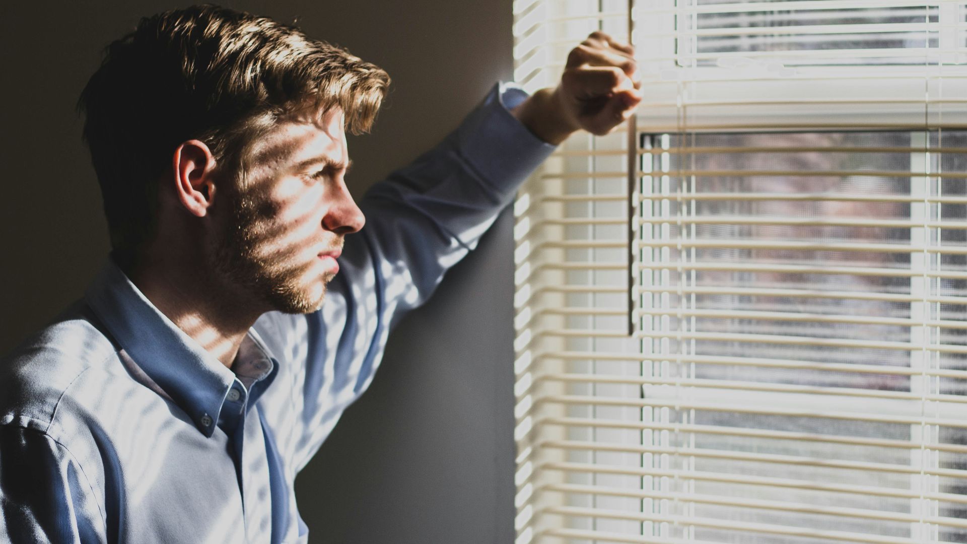 person near clear glass window pane and window blinds low-light photography