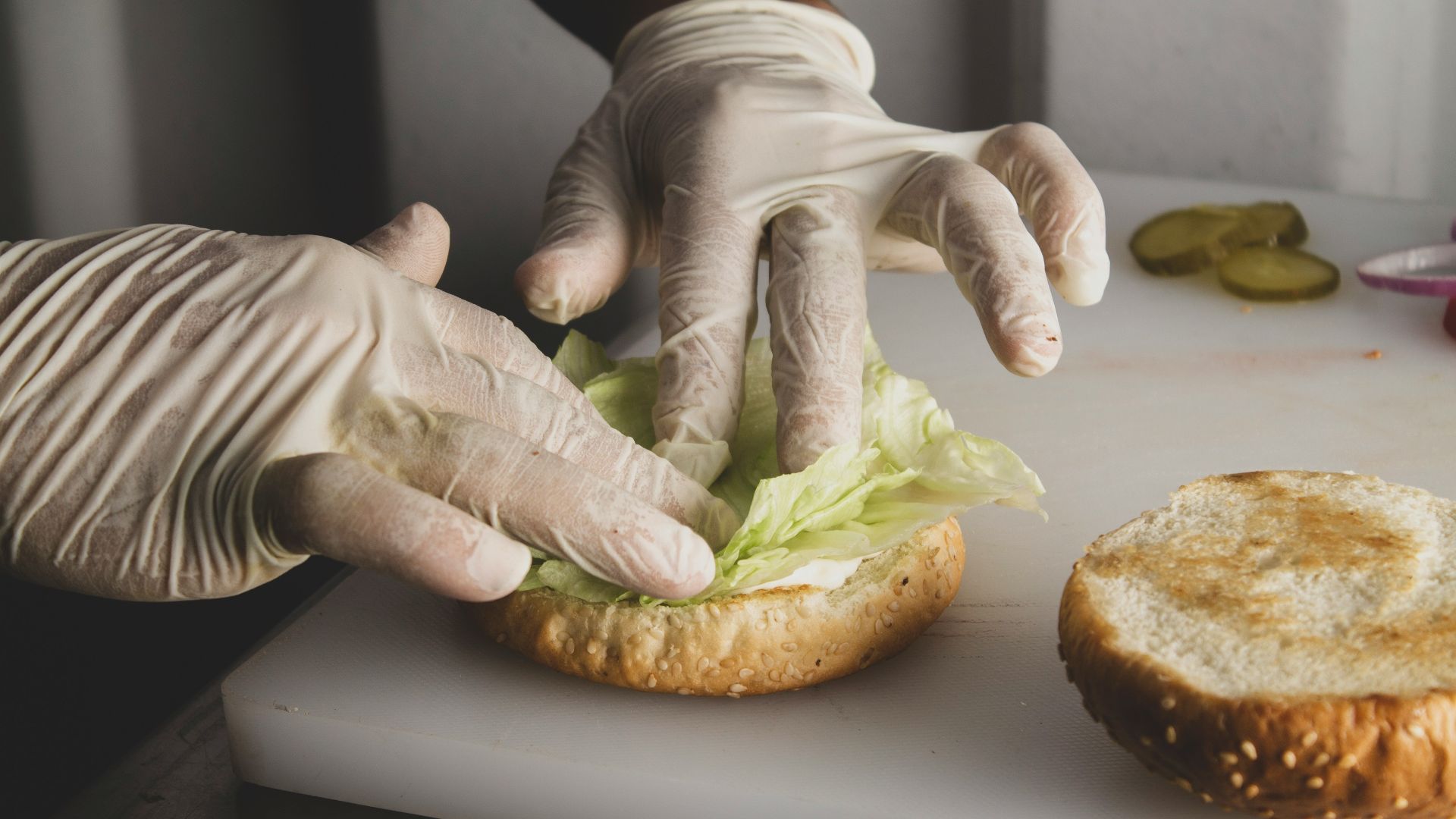 a person in white gloves and gloves preparing a sandwich