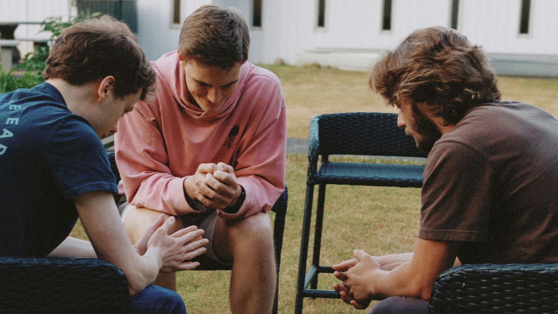 Three young men sitting in a circle praying.