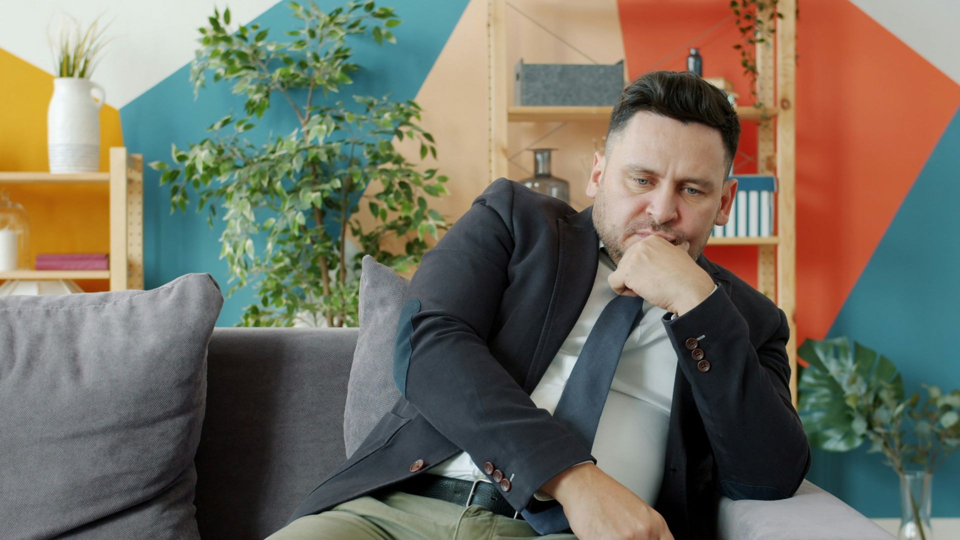Man in suit sitting on couch looking thoughtful.