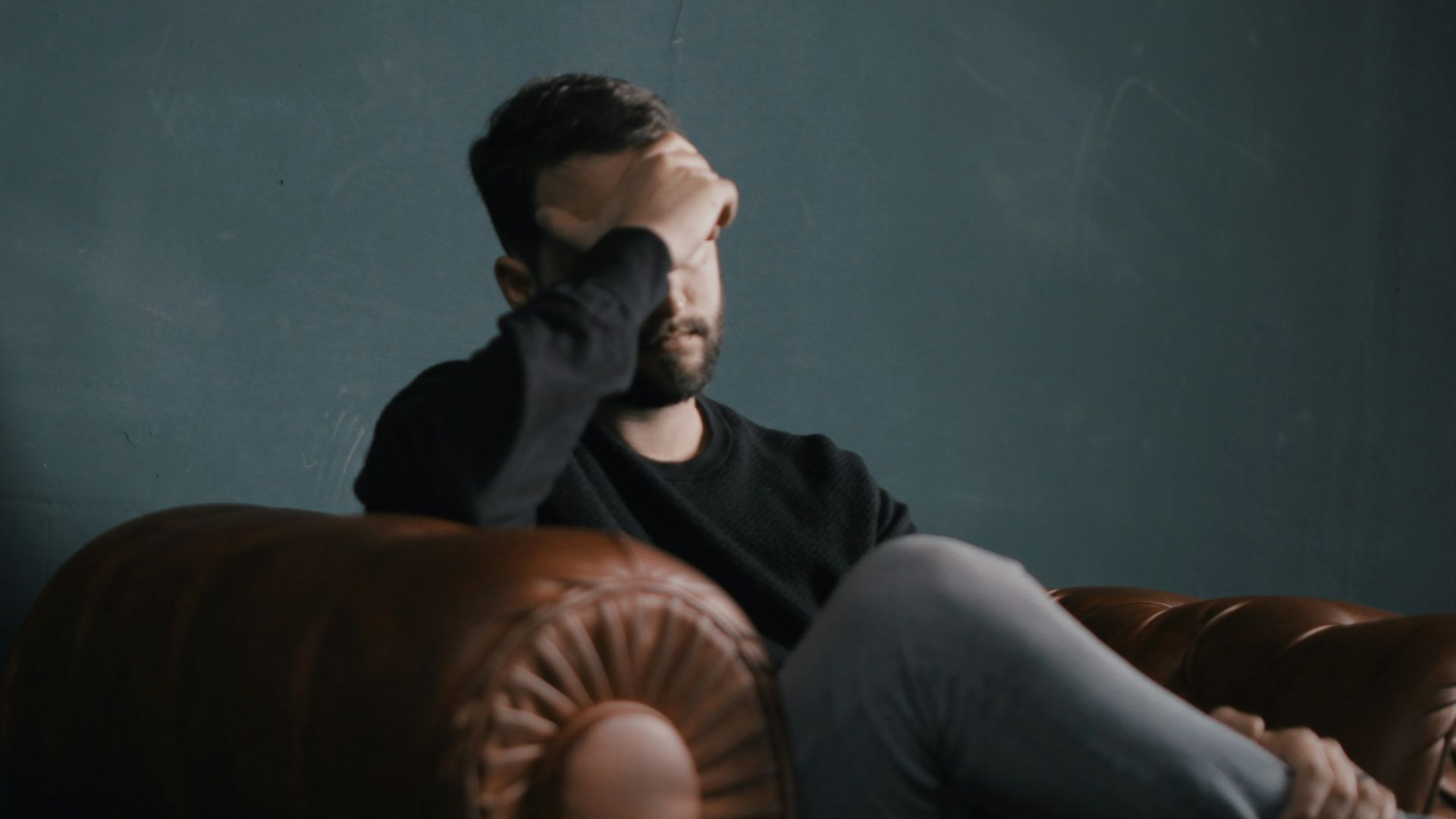 a man holds his head while sitting on a sofa