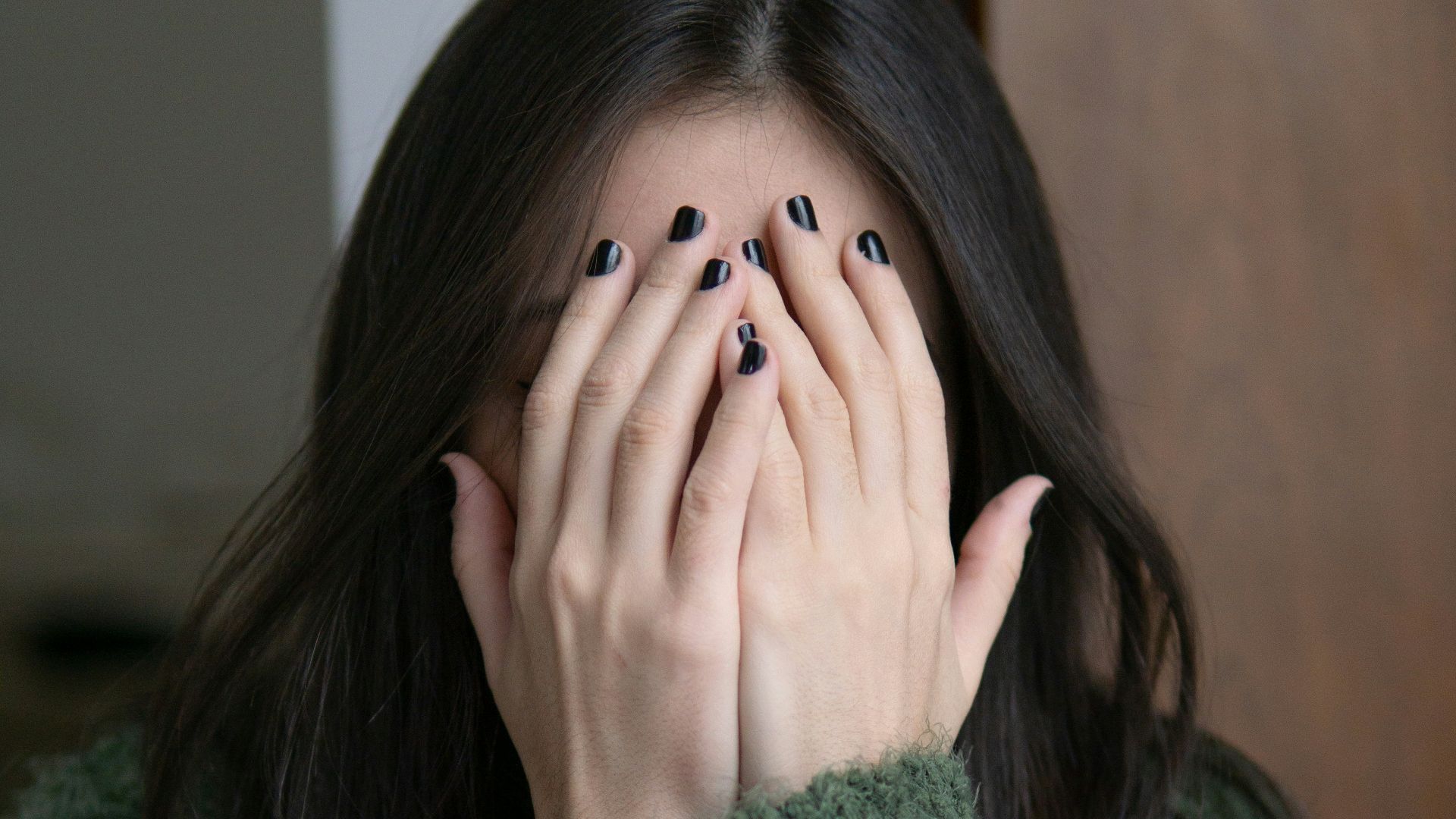 woman in green sweater covering her face with her hand