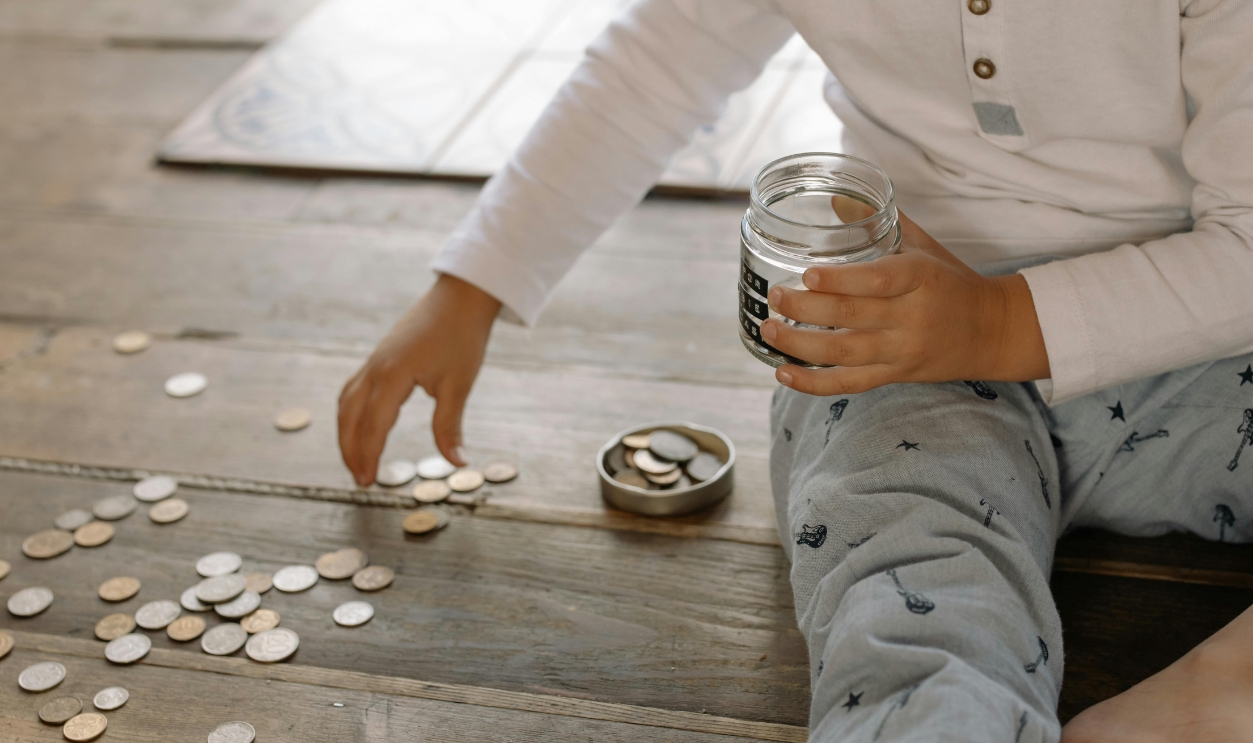 Child Putting Coins Into Glass Jar