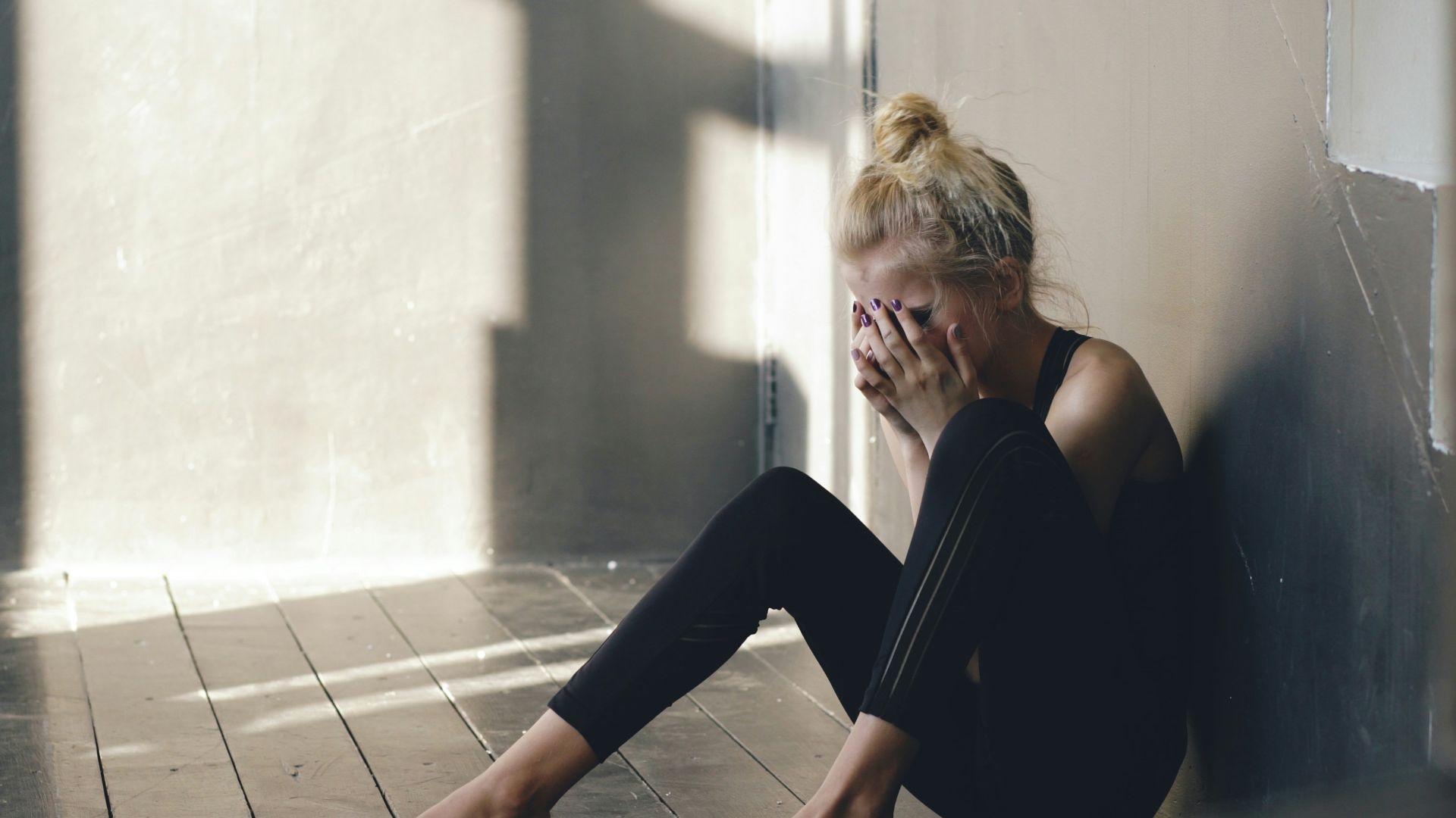 Woman sitting on floor, covering face with hands.