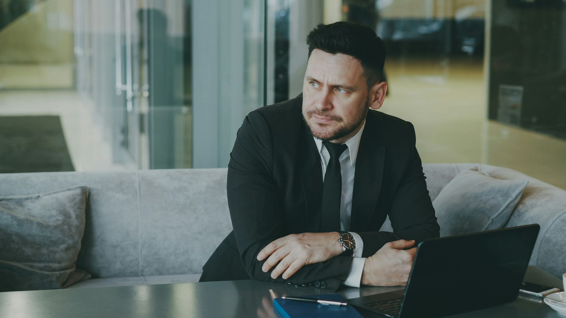 Man in suit sitting at table with laptop and coffee.