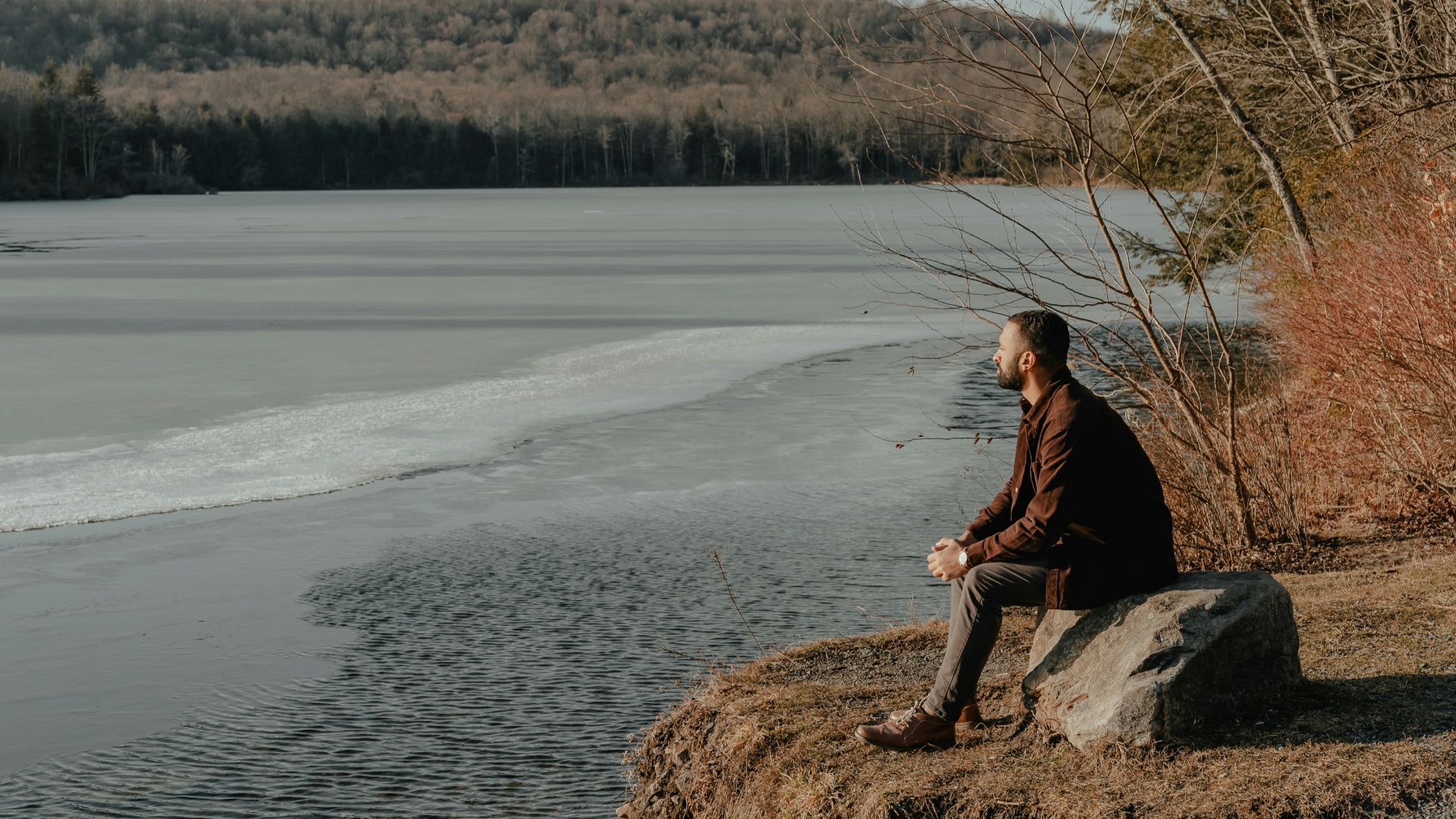 a man sitting on a rock next to a body of water