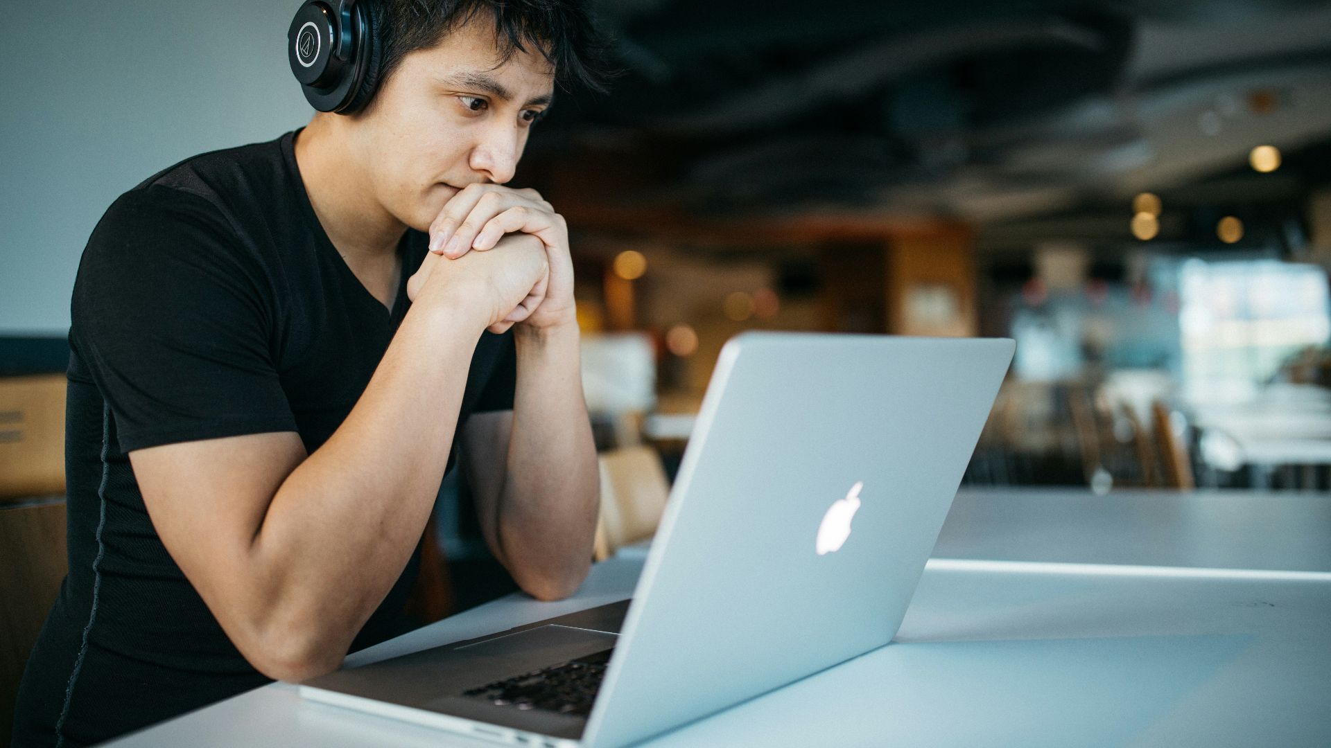 man wearing headphones while sitting on chair in front of MacBook