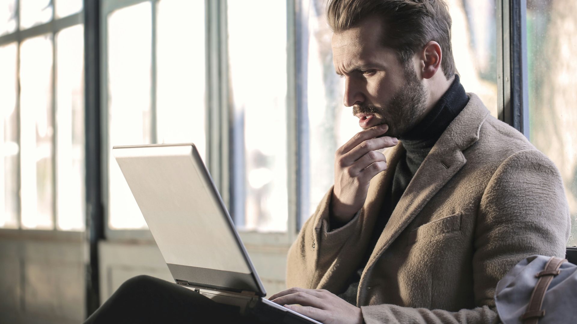 man holding his chin facing laptop computer