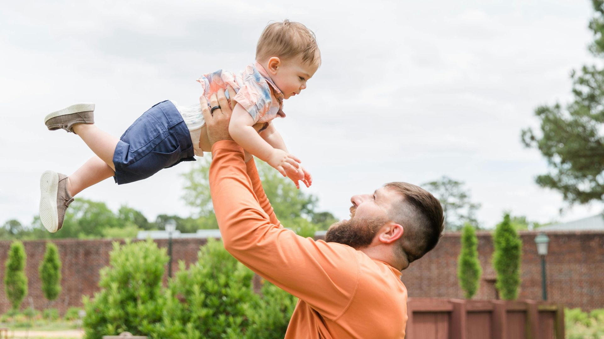 man in orange t-shirt carrying girl in blue denim shorts during daytime