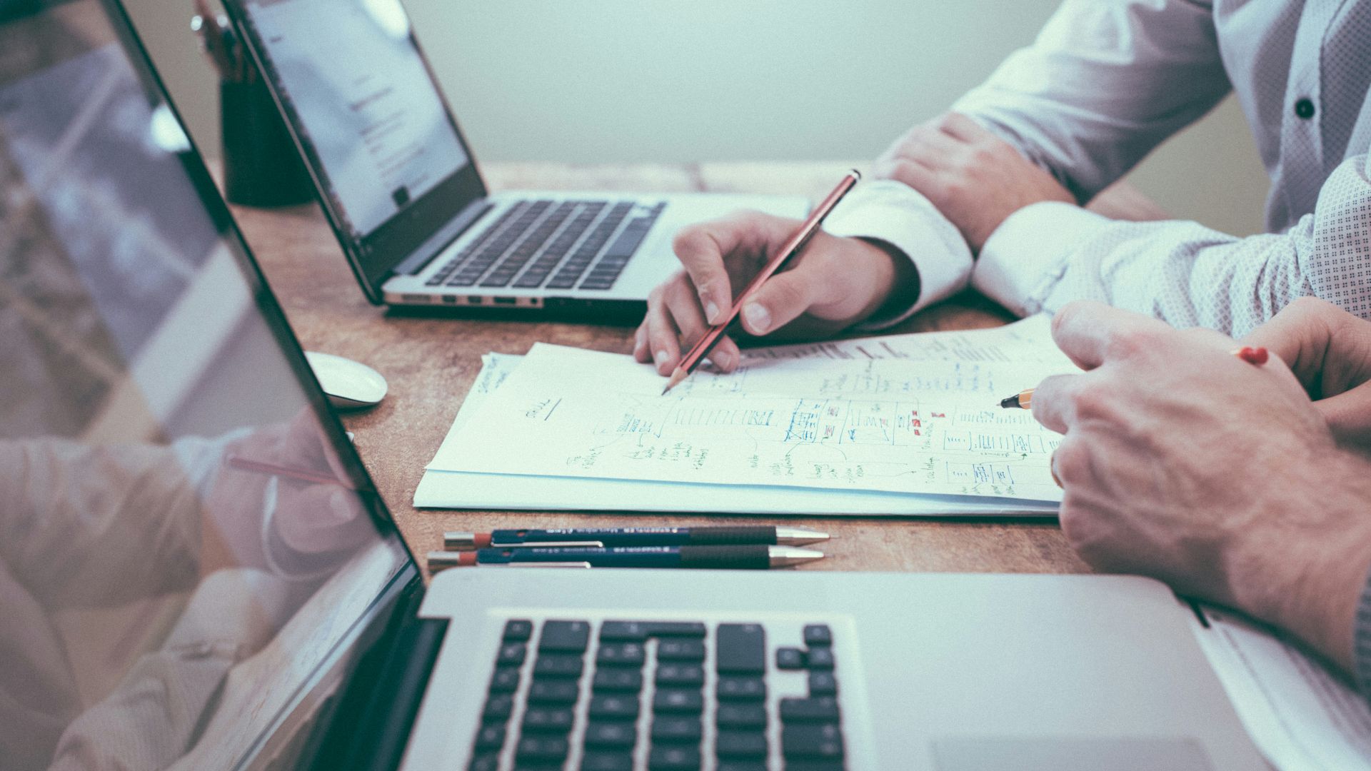 person holding pencil near laptop computer