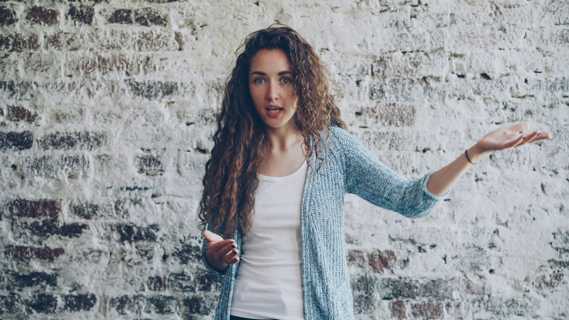 Woman gesturing while speaking against brick wall.