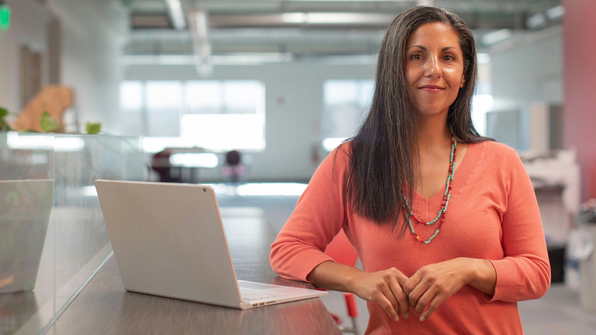 woman in orange long sleeve shirt sitting beside table with macbook pro
