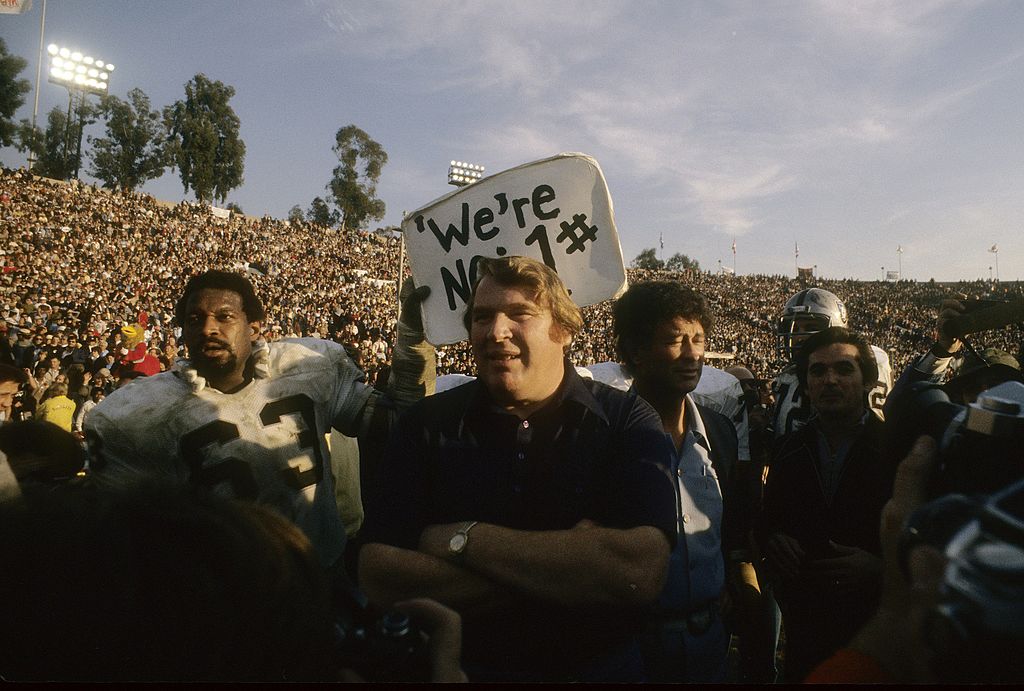 John Madden, head coach of the Oakland Raiders walking off the field with offensive guard Gene Upshaw #63 holding up a sign 