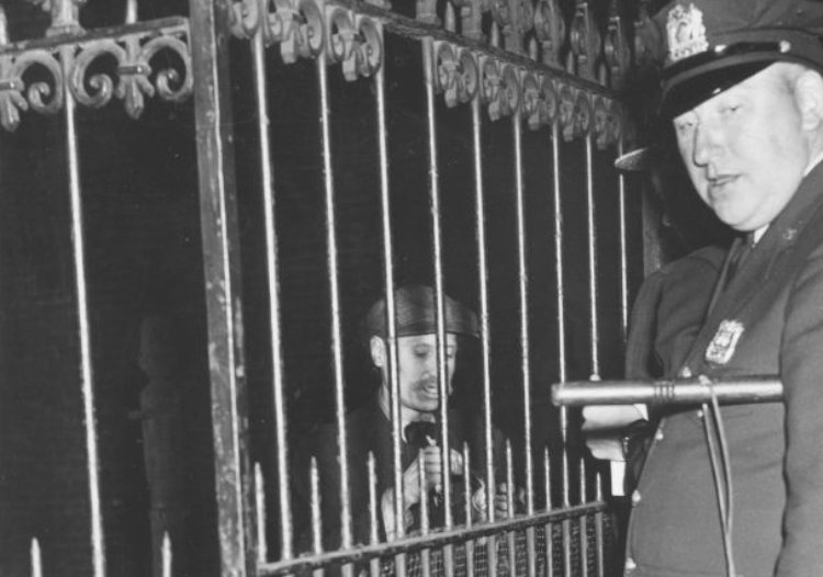 A police officer stands with eccenctric hoarder Langley Collyer (1885 - 1947) (behind fence)