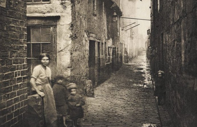 A poor woman with two piteously children in the dirty street in England