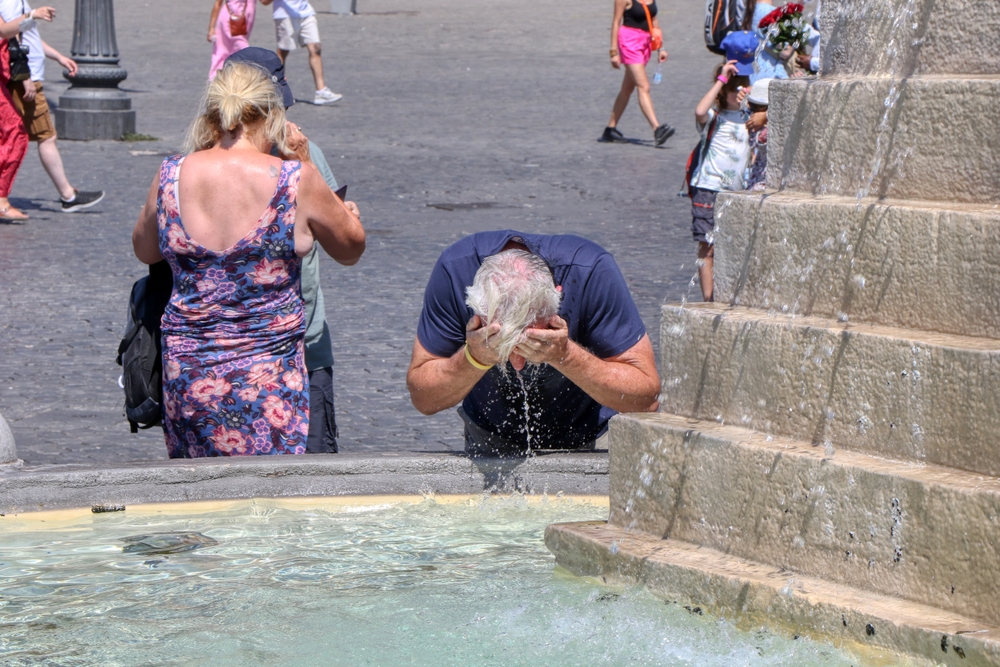 Tourist refreshes his head with water from a fountain