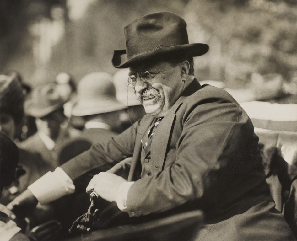 Theodore Roosevelt smiling from an automobile.
