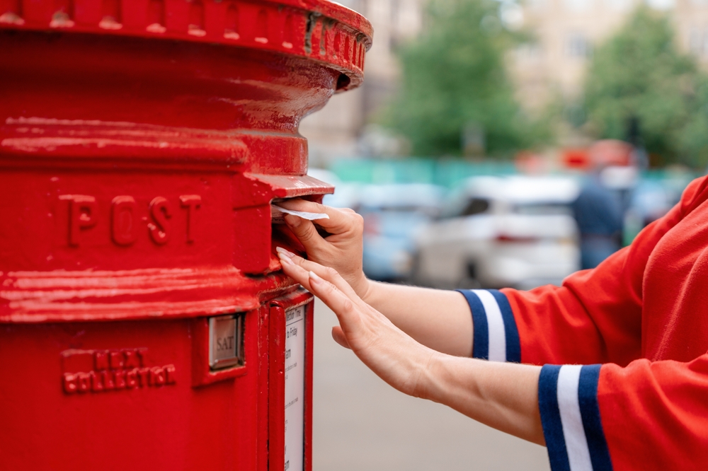 Woman in red short posting letters in red post box