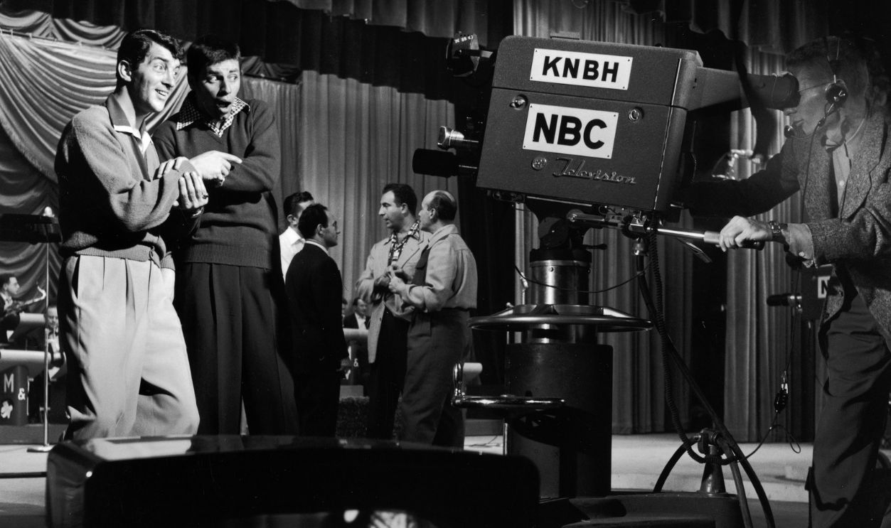 Gettyimages - 3232682, Hollywood Vs TV 2nd February 1952: EXCLUSIVE American comic team Jerry Lewis and Dean Martin (1917 - 1995) performing for the camera on the set of the television show, 'Hollywood vs TV'. A group of men stand talking in the background.