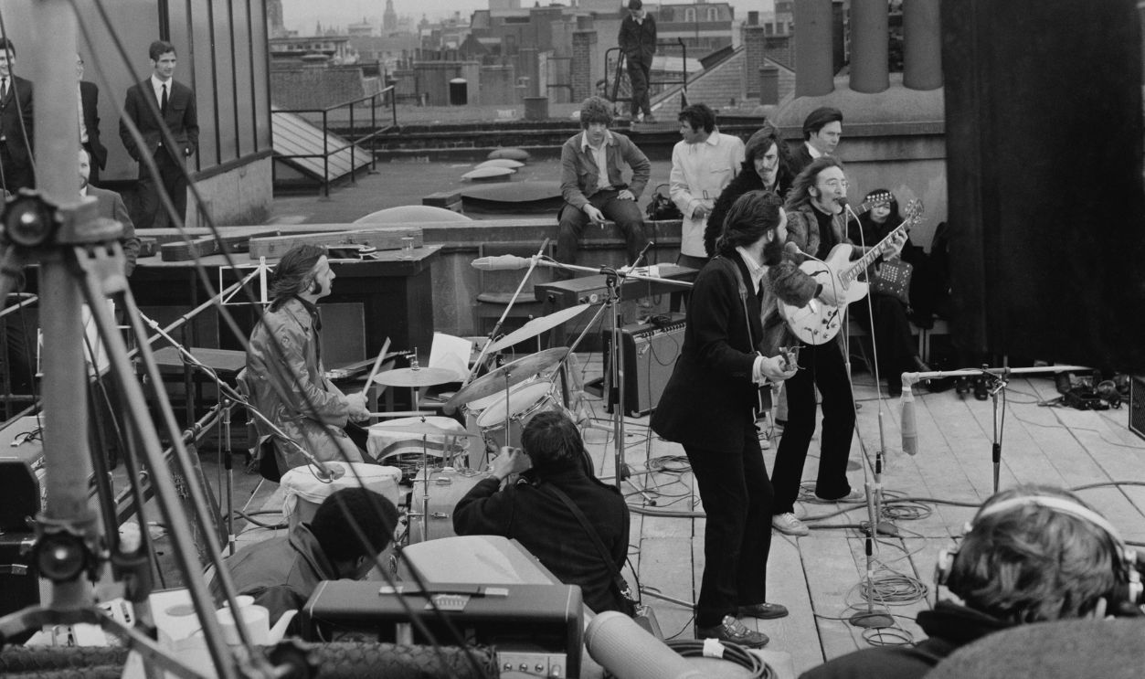 The Beatles' rooftop concert British rock group the Beatles performing their last live public concert on the rooftop of the Apple Organization building for director Michael Lindsey-Hogg's film documentary, 'Let It Be,' on Savile Row, London, UK, 30th January 1969; drummer Ringo Starr sits behind his kit, singer-songwriters Paul McCartney and John Lennon (1940 - 1980) perform at their microphones, and guitarist George Harrison (1943 - 2001) stands behind them. Lennon's wife Yoko Ono sits at right. 