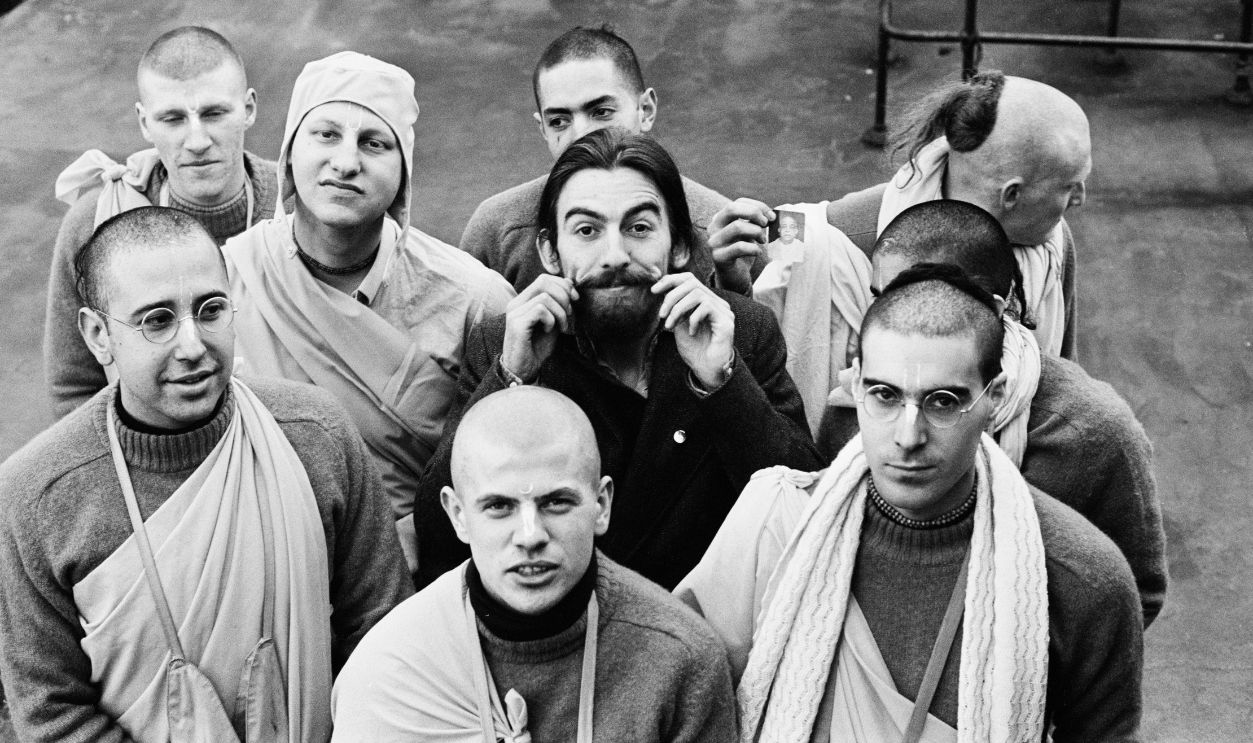 George Harrison, Radha Krishna Temple Members, 1970 Musician George Harrison twirls his moustache while standing with members of Radha Krishna Temple (London) on the roof of the Apple Corps building, Savile Row, London, March 5th 1970. Harrison produced a single by the group. 
