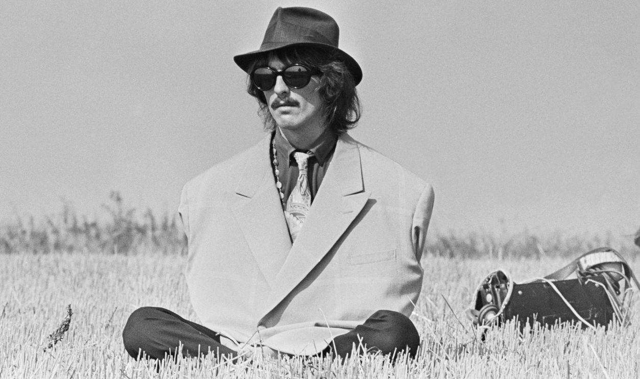 Filming Magical Mystery Tour George Harrison (1943-2001), guitarist with the Beatles, pictured wearing an oversized jacket and a trilby hat during filming of 'Magical Mystery Tour' in a field near Newquay in Cornwall on 14th September 1967. 