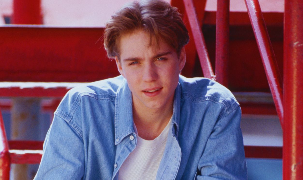 Gettyimages - 635762349, Portrait of Jonathan Brandis (Original Caption) : 1994- Picture shows actor Johnathan Brandis posed sitting on steps outside. He is wearing a pair of jeans and a denim shirt. His arms are resting on his legs and his hands are touching.