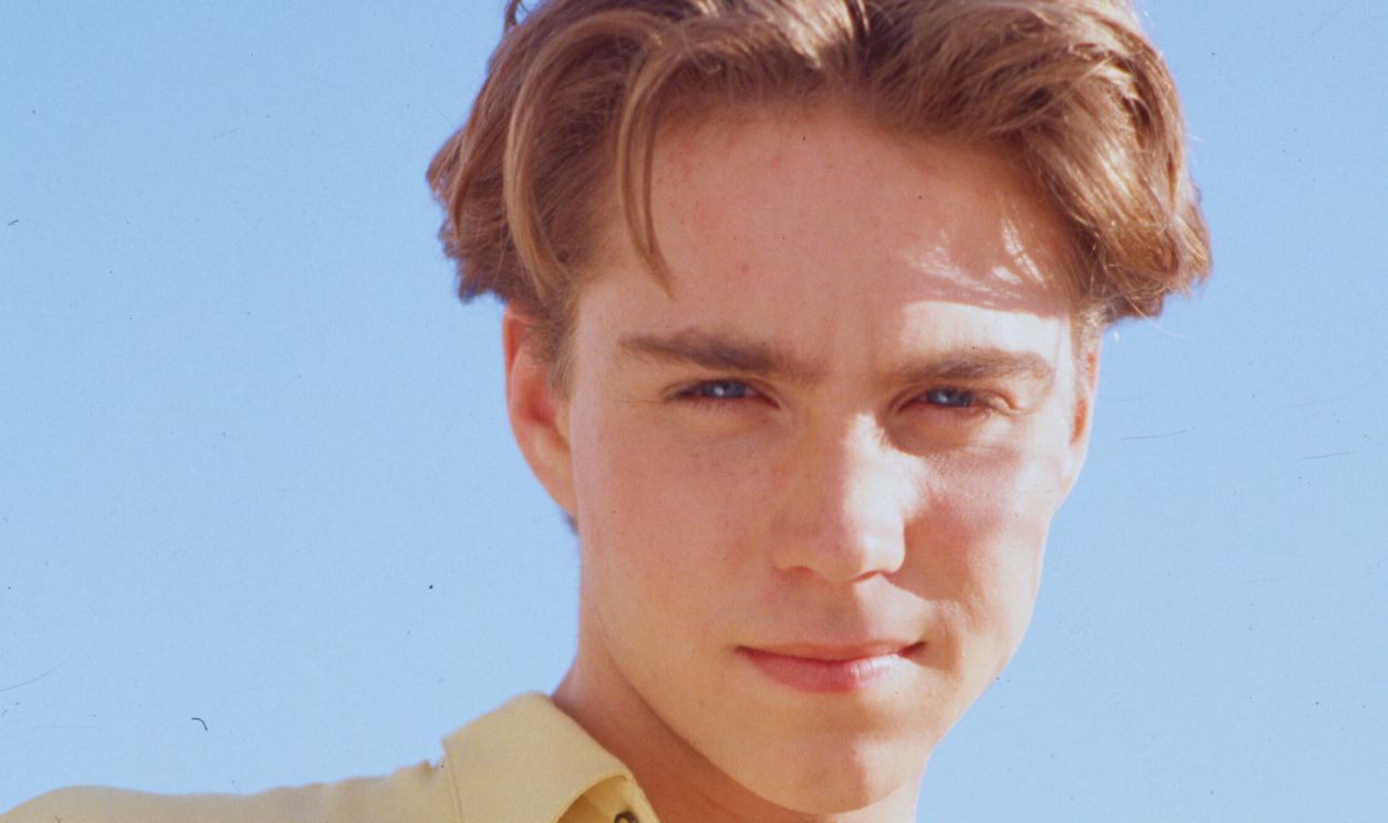 Gettyimages - 635762355, Jonathan Brandis Buttoning a Shirt (Original Caption) : 194-Los Angeles,CA- Picture shows actor Johnathan Brandis posing outside while buttoning a yellow shirt. He is looking down into the camera.