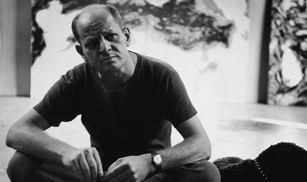 American abstract expressionist painter Jackson Pollock (1912 - 1956) sits with a black dog, possibly a curly coated retriever, in his studio at 'The Springs,' East Hampton, New York, August 23, 1953.