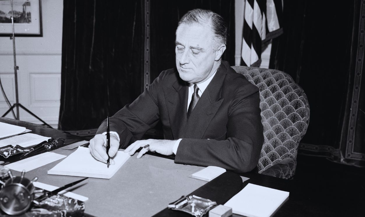 Gettyimages - 1354397626, President Franklin Roosevelt sitting at a desk and signing a piece of paper ca. 1934 President Franklin Roosevelt sitting at a desk and signing a piece of paper ca. 1934.
