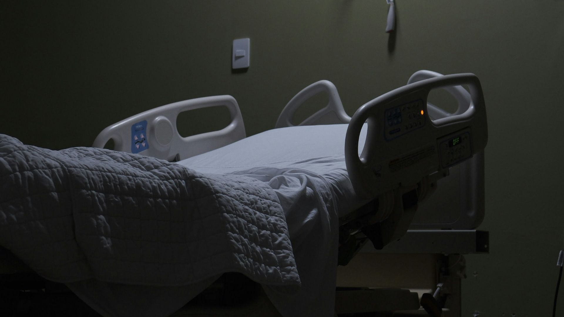 An empty hospital bed sits in a dimly lit room.