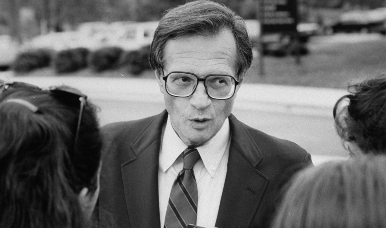 TV host Larry King outdoors surrounded by people during Democratic Convention.