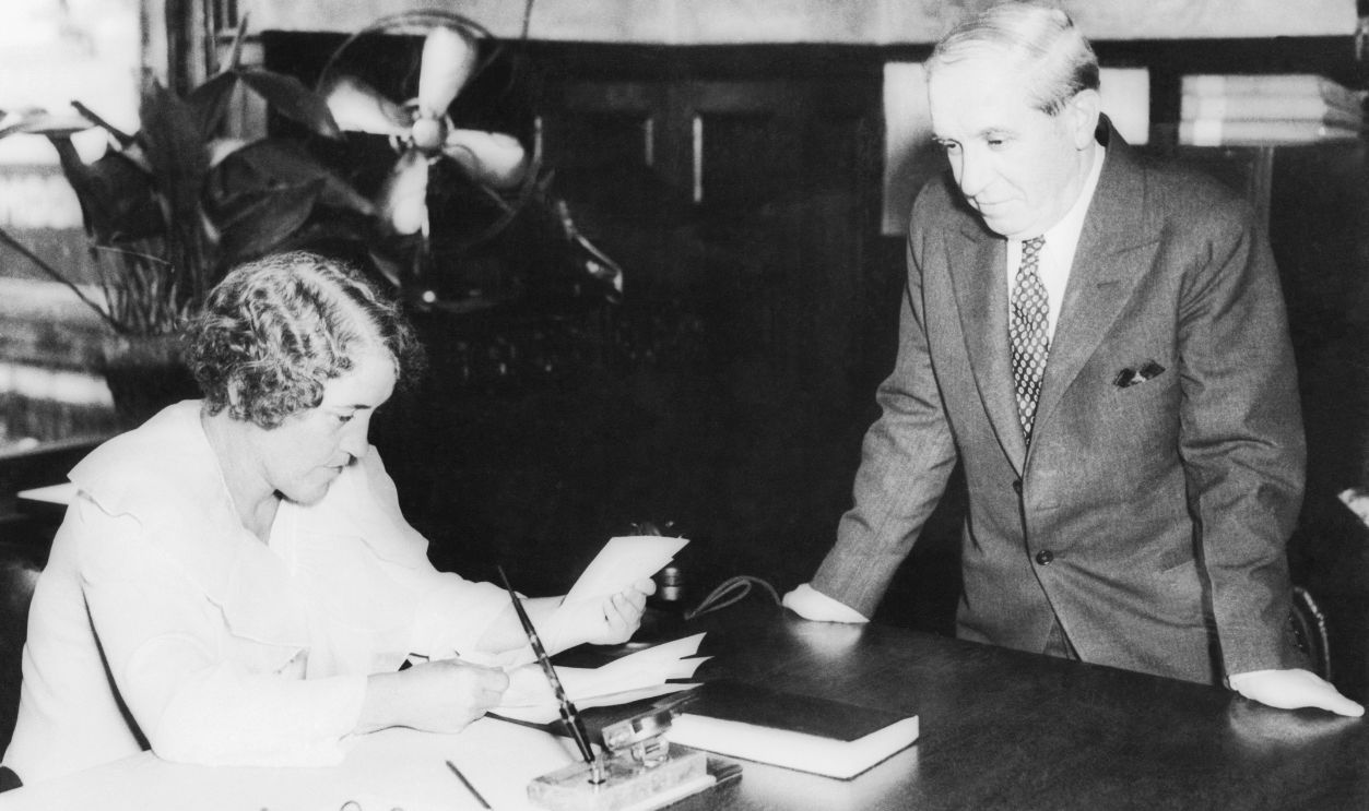 Charles Ponzi's last hopes of blocking deportation to Italy disintegrated on July 12th at Boston, MA as completely as he bubble of 1920. Governor Ely denied his petition for a full pardon, on which the wizard of illegal finance based his hopes of being permitted to remain in this country. After a state house hearing before the governor, dramatized by Ponzi's own eloquent plea and the tears of his wife, Mrs. Rose Ponzi, they kissed, and Ponzi started for the immigration station at East Boston, where he is here shown surrendering to immigration Commissioner, Mary Ward, and was at once locked up.