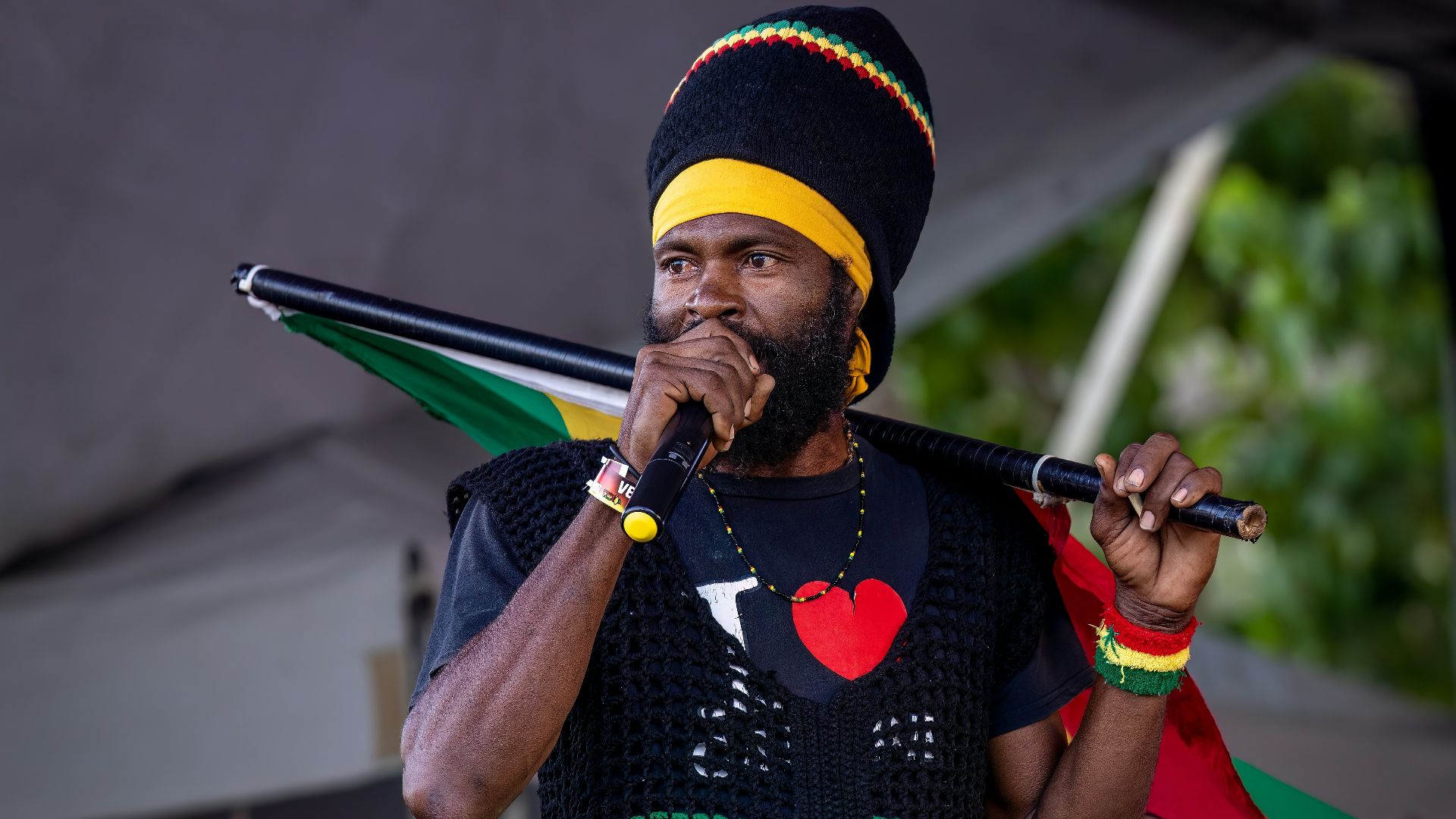 A rastafarian man speaks on stage with a flag.
