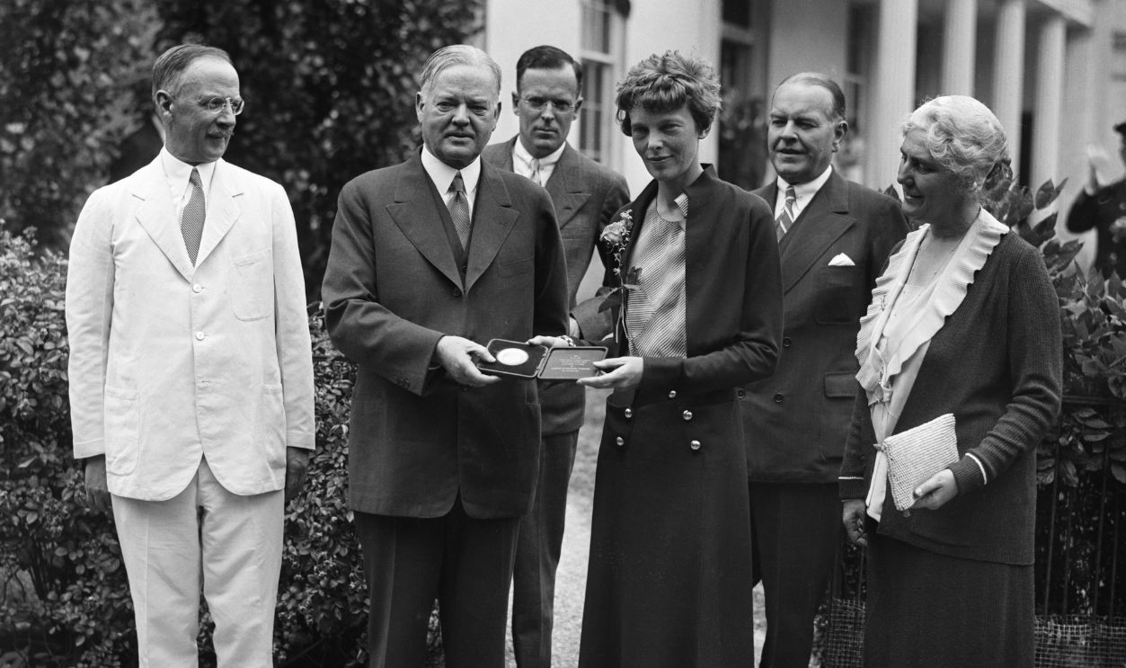 President Herbert Hoover presenting the National Geographic Society gold medal to Amelia Earhart in recognition of her continuous solo flight across the Atlantic. Front row from left: Dr. Gilbert Grosvenor, National Geographic Society; President Herbert Hoover; Amelia Earhart; First Lady Lou Henry Hoover. Back row from left George Palmer Putnam, husband of Amelia Earhart; John La Gorce, National Geographic Society.