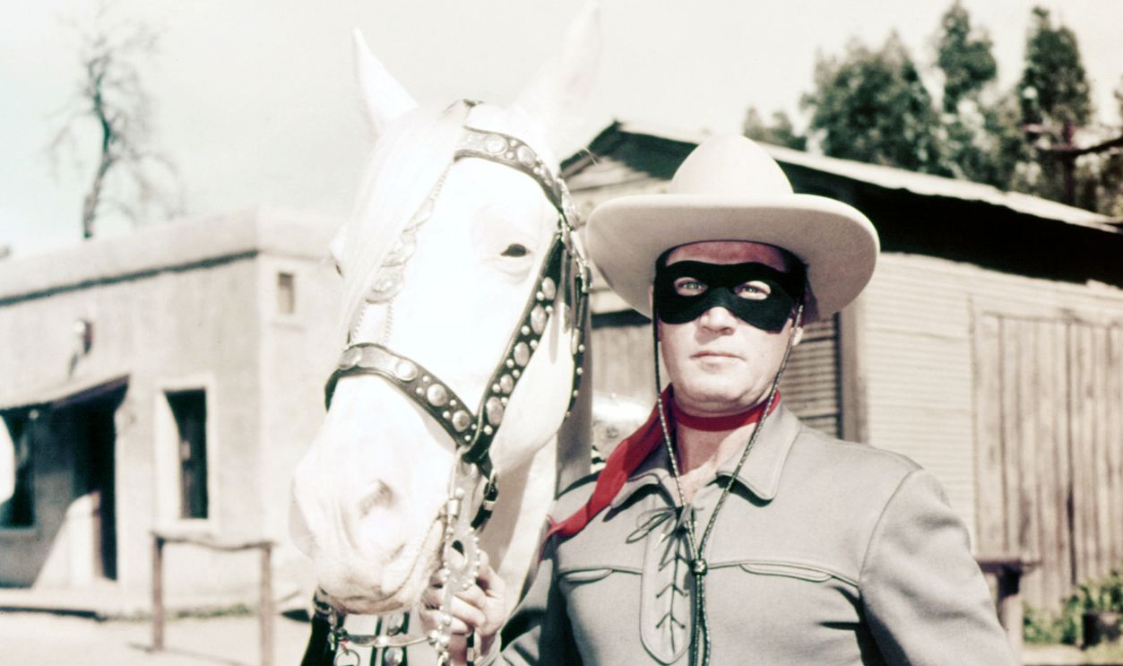 Clayton Moore (1914-1999), US actor, in costume, holding the reigns of his horse, Silver, in a publicity still issued for the television series, 'The Lone Ranger', USA, circa 1950. The adventure series starred Moore as 'The Lone Ranger'.