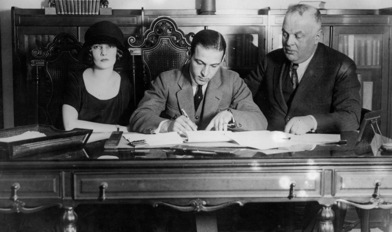 Gettyimages - 2642525, Rudolph Valentino Rudolph Valentino (1895 - 1926), the Italian-American leading man and great romantic idol, signing a contract, accompanied by his wife.