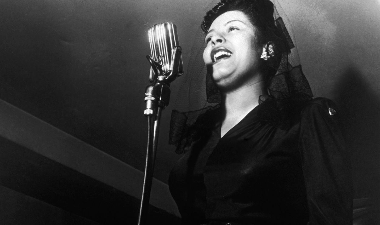 American jazz singer Billie Holiday (1915 - 1959) sings in front of a microphone at a Sunday afternoon jam session at Ryan's on 52nd Street, New York City. 