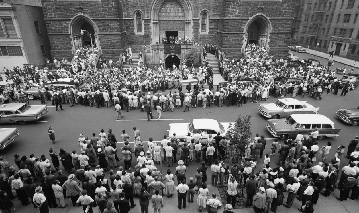 NY- Crowds mill around St. Paul the Apostle Roman Catholic Church as the casket of blues singer Billie Holiday is brought out following a solemn requiem mass. Miss Holiday died from heart failure brought on by congestion of the lungs. She had been hospitalized for more than six weeks.