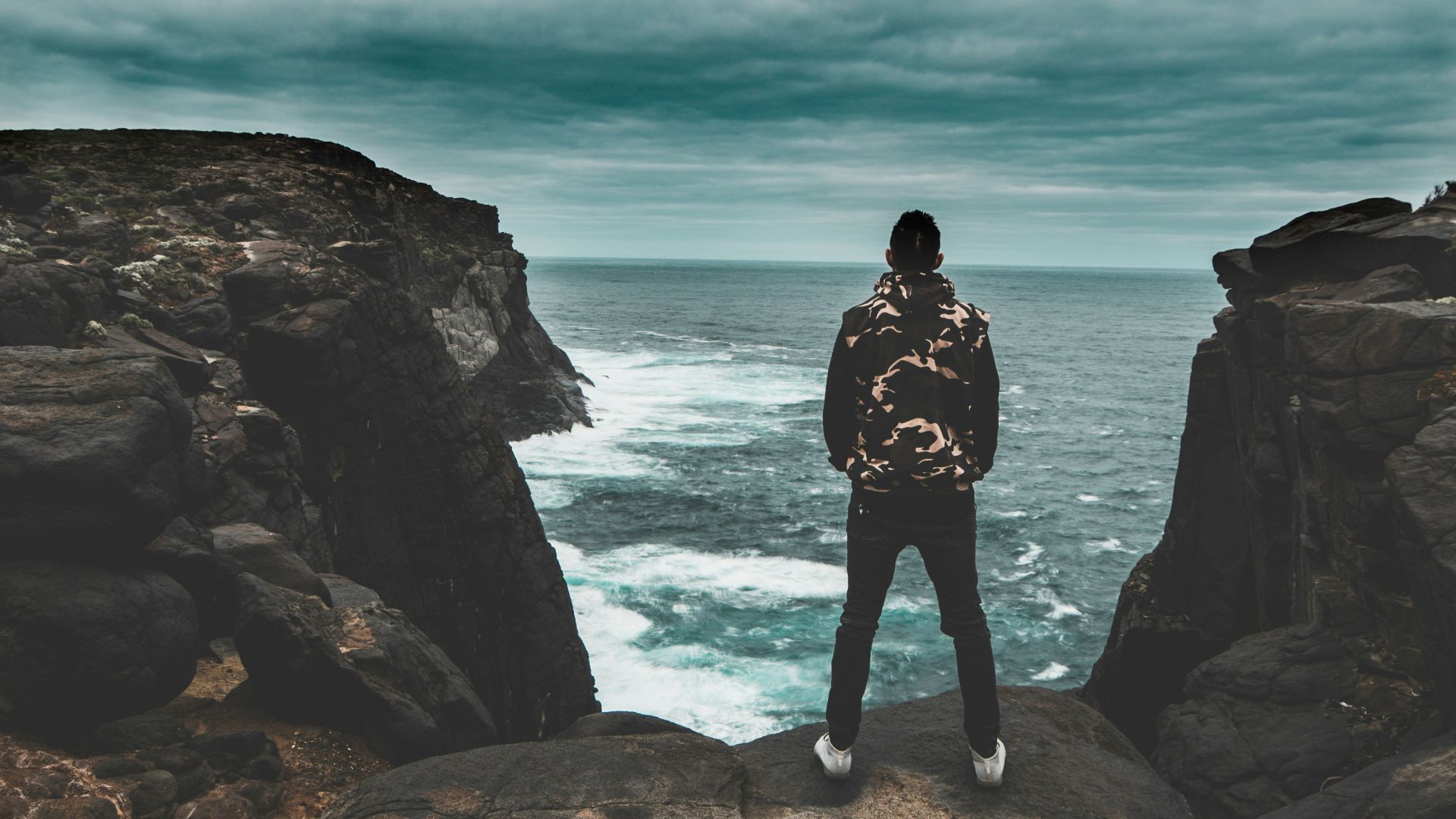 woman in black dress standing on rock formation near body of water during daytime
