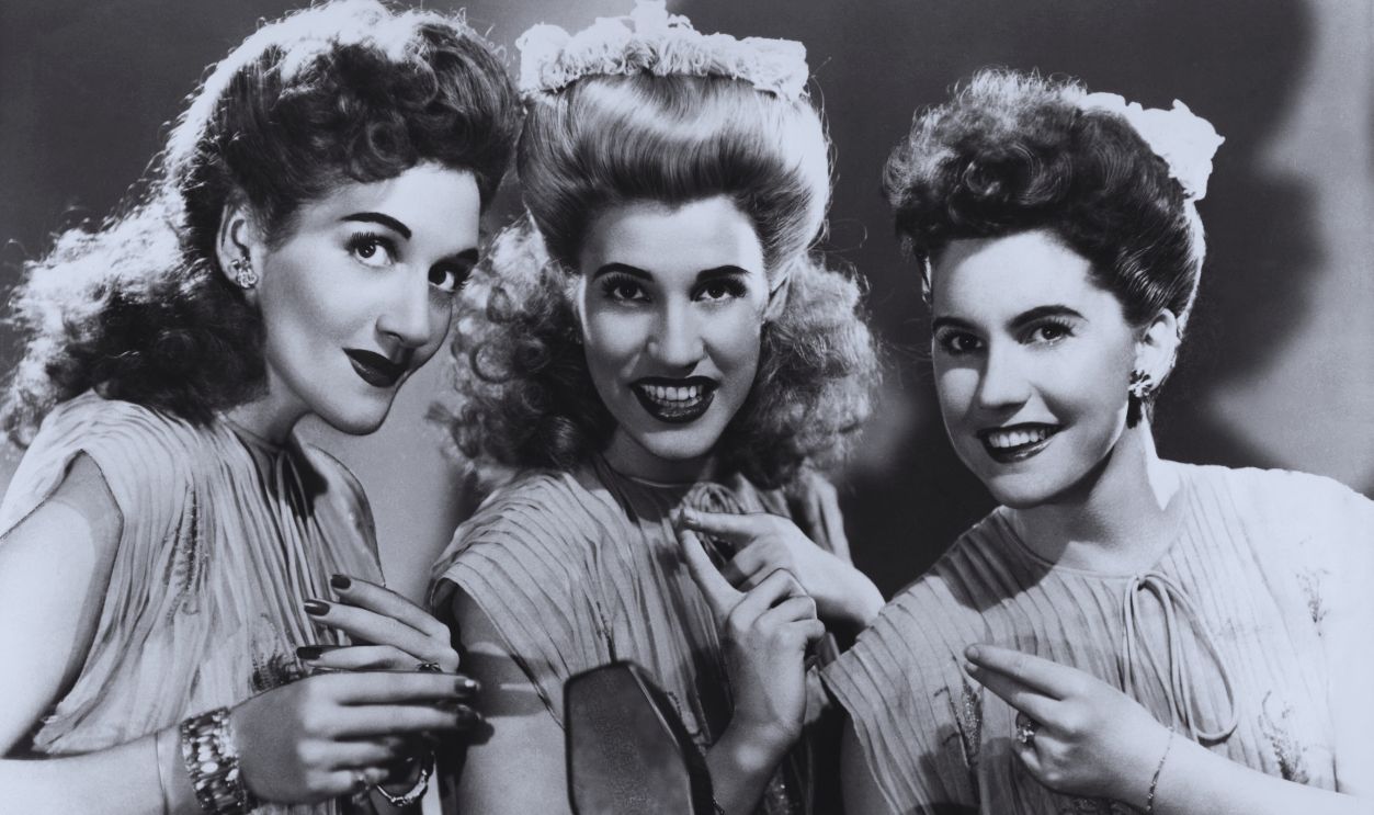 Gettyimages - 103013123, Andrews Sisters The Andrews Sisters (LaVerne Sophia Andrews (1911-1967), Patricia Marie Andrews and Maxene Angelyn Andrews (1916-1995)) smiling wearing matching outfits around a microphone, USA, circa 1940.