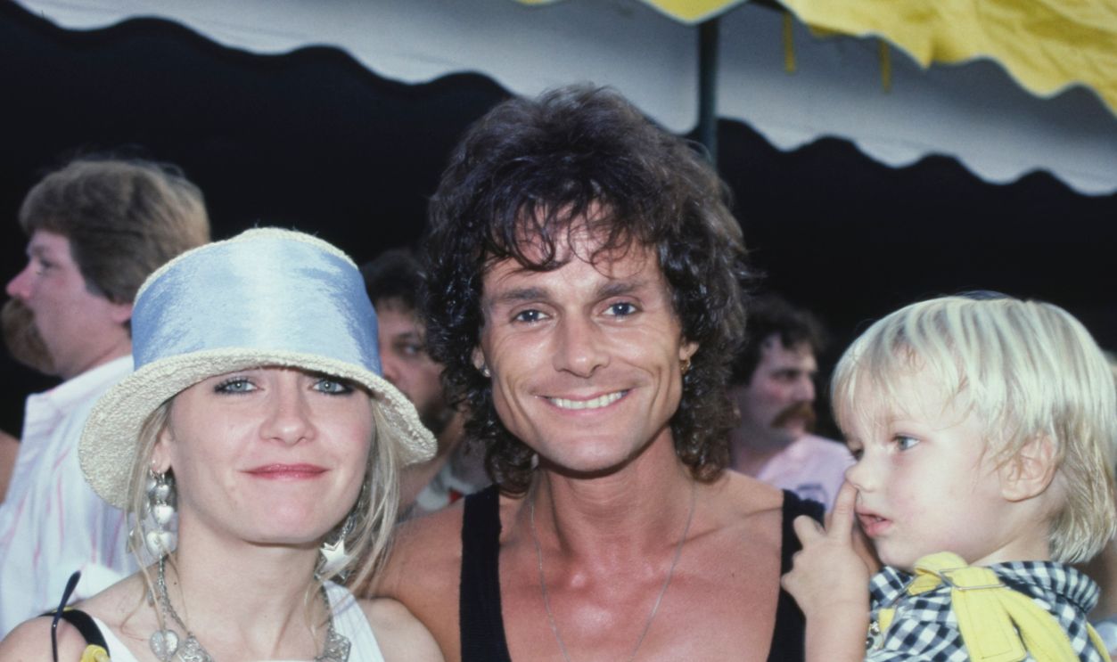 British actor and singer Michael Des Barres, wearing a black ves, with his wife, Pamela and son, Nicholas, backstage at the Live Aid benefit concert, held at the John F Kennedy Stadium in Philadelphia, Pennsylvania, 13th July 1985.