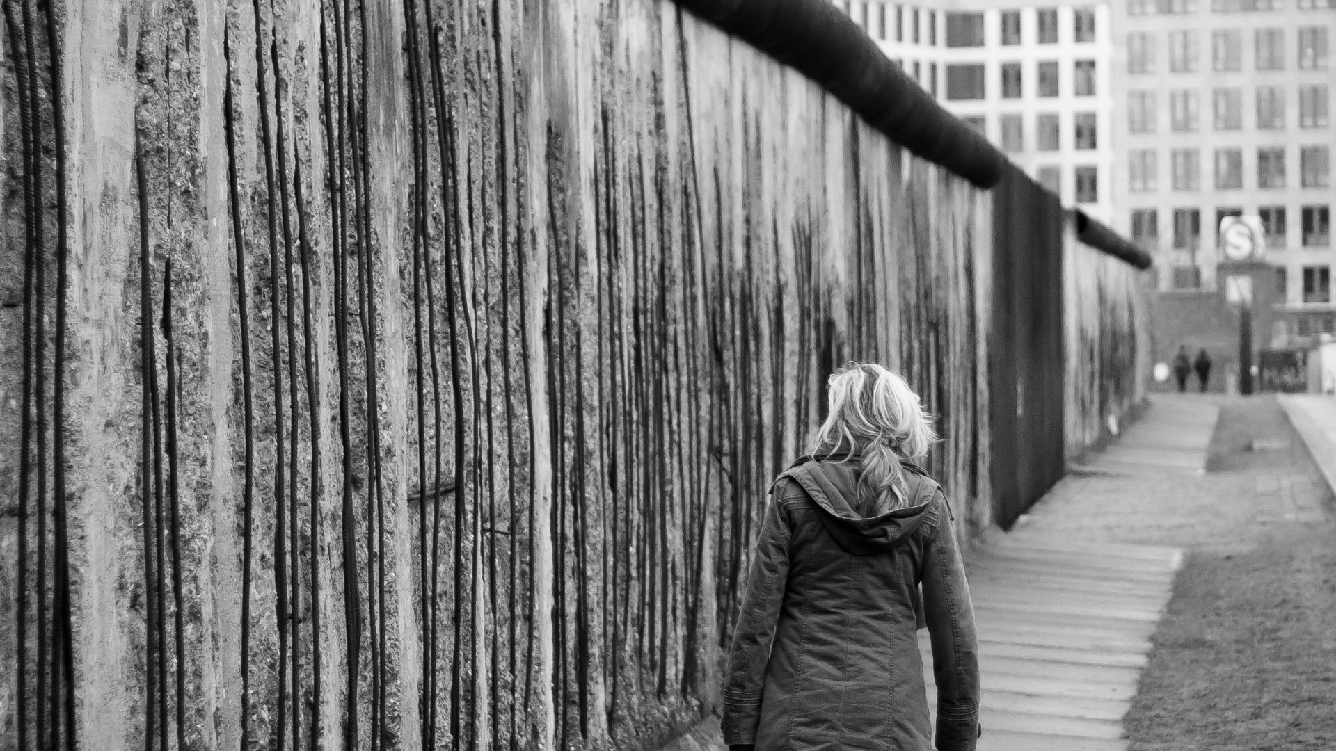 grayscale photo of woman walking on sidewalk