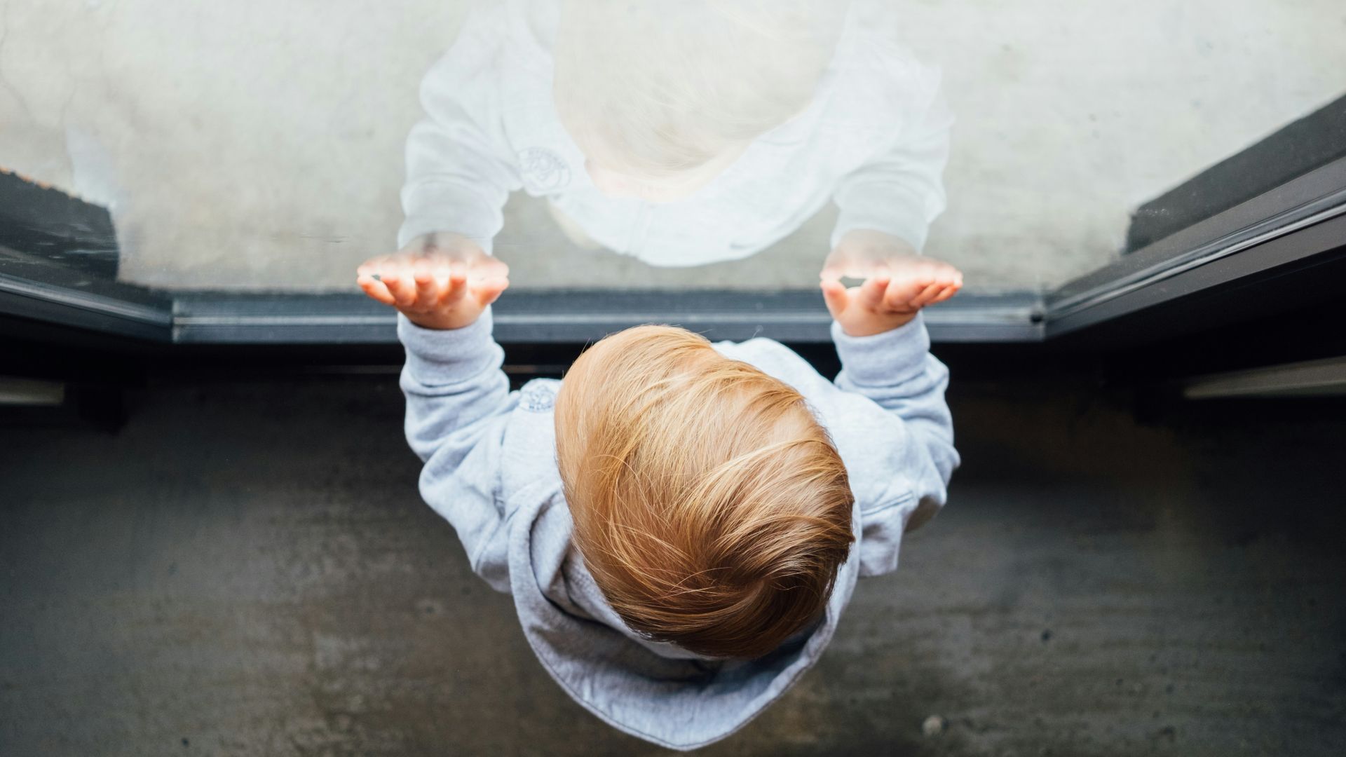 blonde haired boy in grey top leaning on glass door