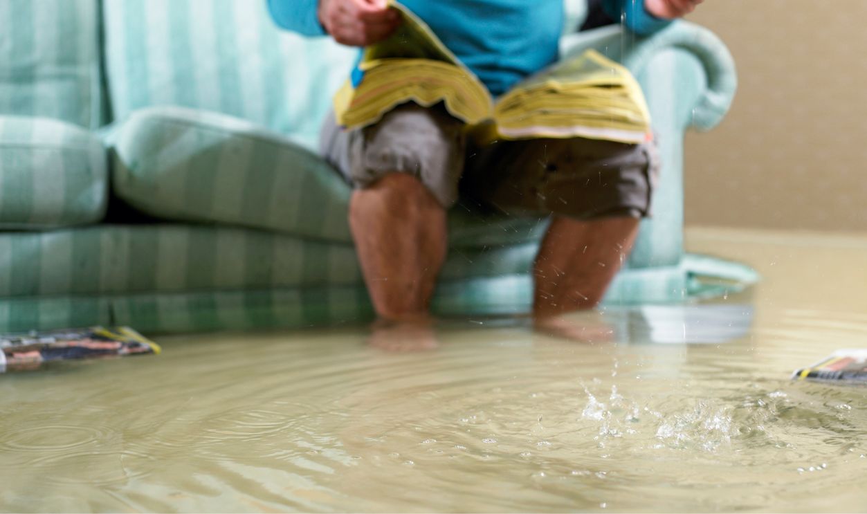 Man sitting in flooded living room using phone, low section